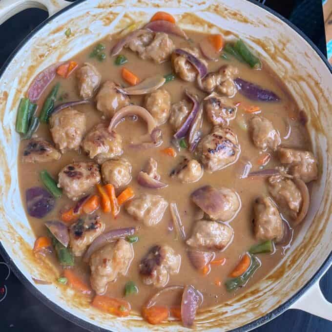 Satay Sausage Rice Bowl A pan filled with meatballs, sliced carrots, green beans, and red onions in a thick brown sauce.