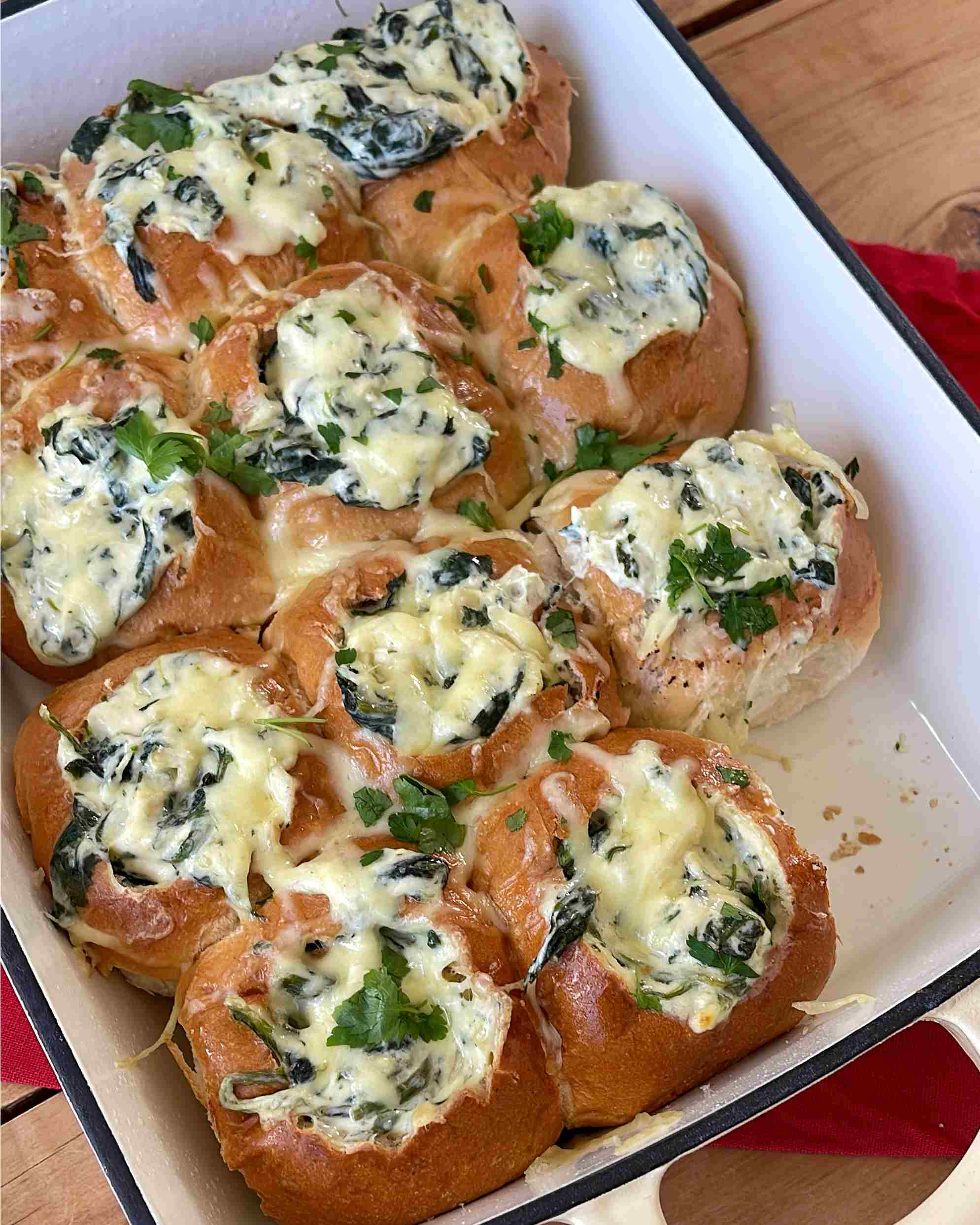 Creamy Spinach Cob Sliders A baking dish filled with golden brown bread rolls topped with spinach, melted cheese, and chopped herbs.