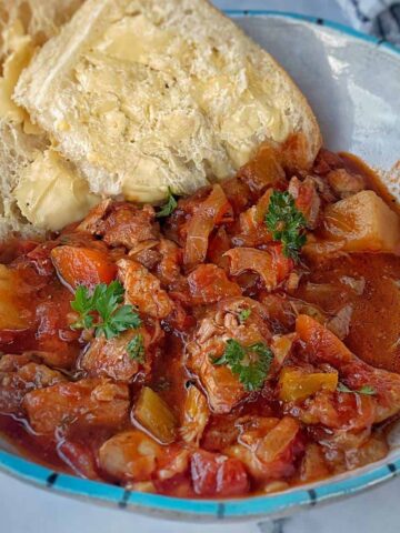 A bowl of beef stew with vegetables, garnished with parsley, served with two slices of buttered bread.