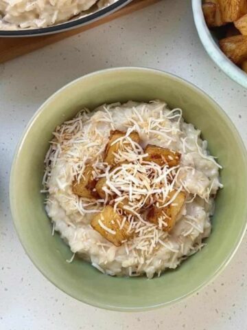 A bowl of creamy rice pudding topped with toasted coconut flakes and caramelized pineapple chunks on a light countertop.