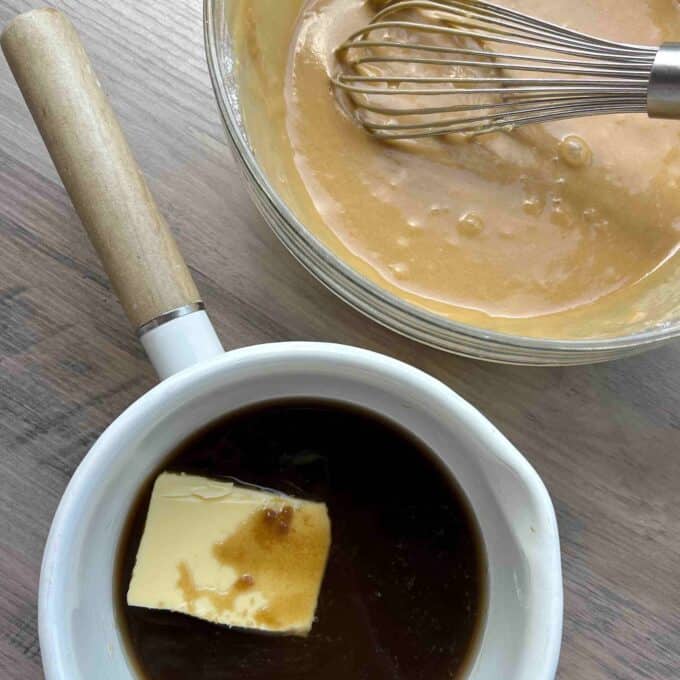 Caramel Apple Sponge Pudding A mixing bowl with batter and a whisk next to a saucepan containing butter and brown liquid on a wooden surface.