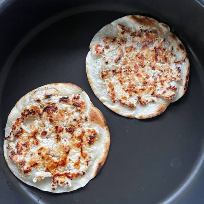Homemade McChicken Tacos Two flat, round breads with browned, crispy tops are cooking in a dark nonstick pan.