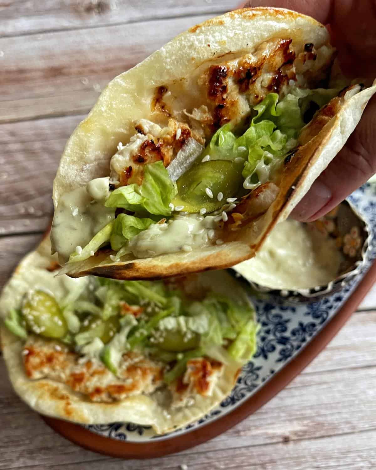 Homemade McChicken Tacos Two grilled chicken tacos with lettuce, pickles, sesame seeds, and creamy sauce in soft tortillas, served on a decorative plate.