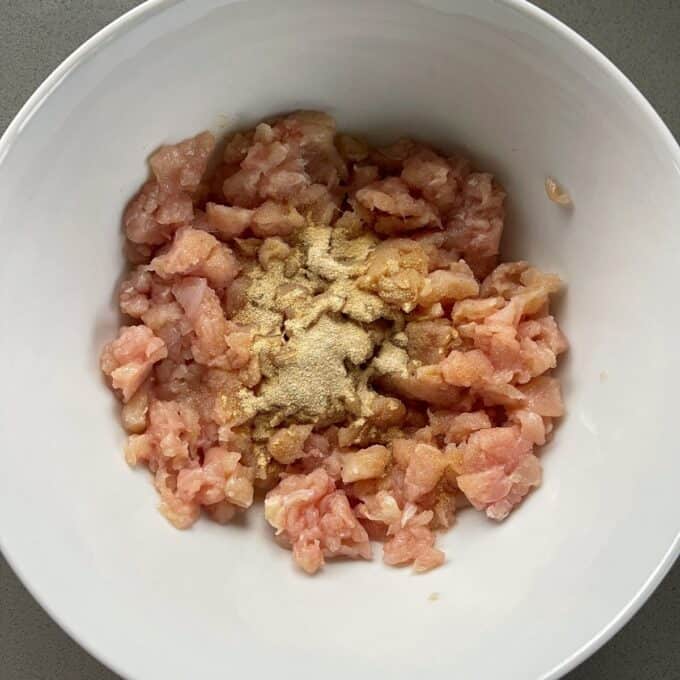 Homemade McChicken Tacos A white bowl containing raw minced chicken topped with ground spices on a gray surface.