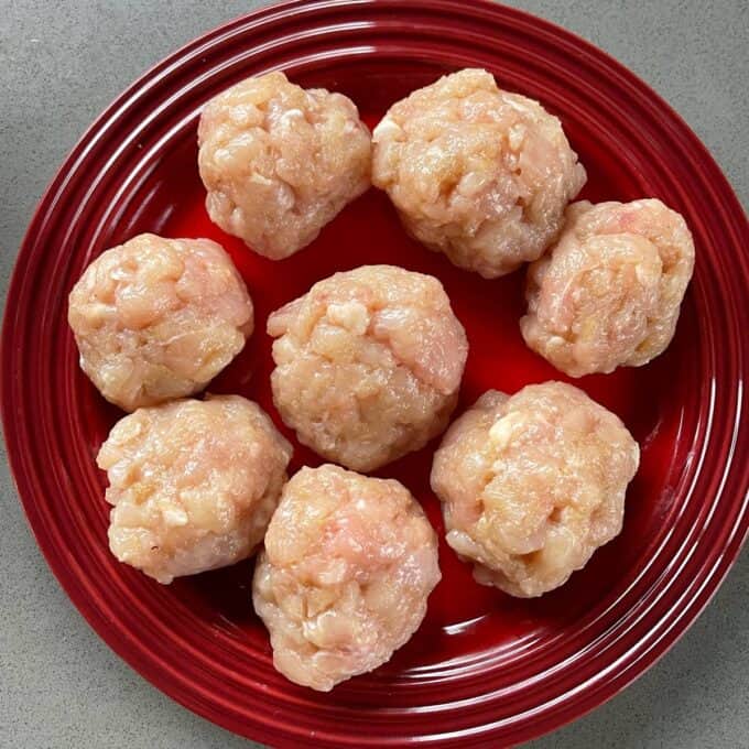 Homemade McChicken Tacos Eight raw ground chicken meatballs arranged on a red plate, placed on a gray surface.