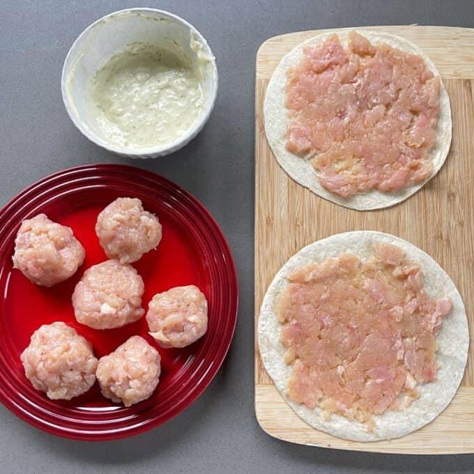 Homemade McChicken Tacos Ground chicken is shaped into balls on a red plate and spread onto two tortillas on a wooden board; a bowl of creamy mixture is nearby.