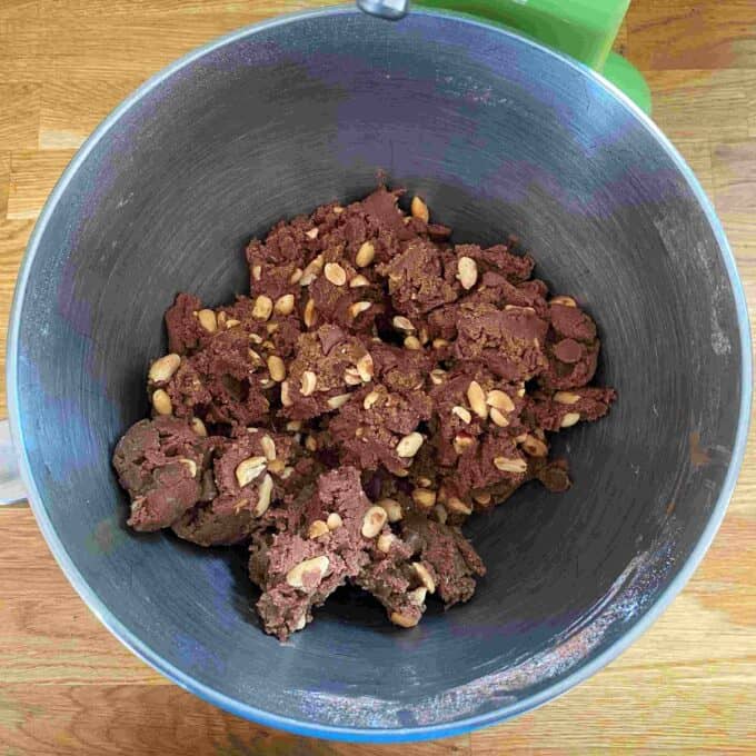 Peanut Brownies A mixing bowl containing chocolate cookie dough with visible peanuts on a wooden countertop.