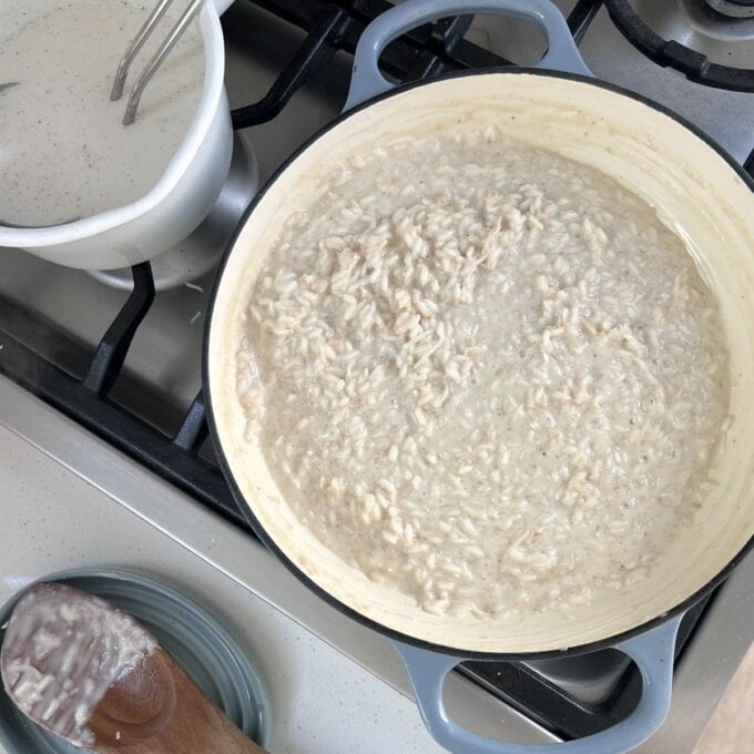 Piña Colada Rice Pudding A pot of oatmeal cooking on a stove, with a mixing spoon resting on a plate and a bowl of liquid mixture nearby.