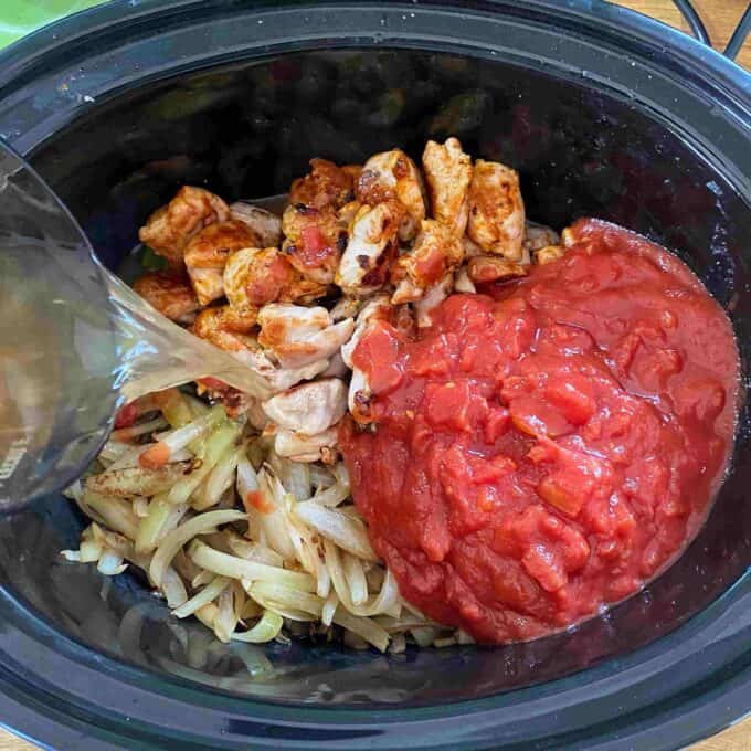 Slow Cooker Tomato Chicken Thigh Stew Sliced onions, seasoned chicken pieces, and diced tomatoes in a slow cooker, with liquid being poured over the ingredients.