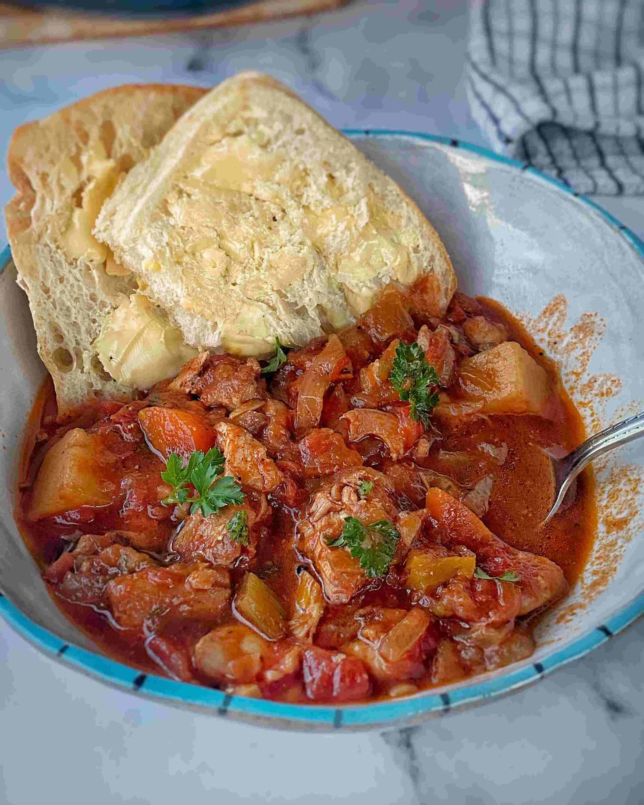 A bowl of beef stew with potatoes and vegetables, garnished with parsley, served with two slices of buttered bread.