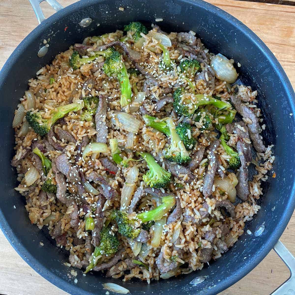 Beef and Broccoli Fried Rice A skillet filled with beef stir fry, broccoli, onions, and rice, topped with sesame seeds.