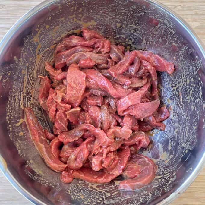 Beef and Broccoli Fried Rice A stainless steel bowl containing raw, marinated strips of beef on a wooden surface.