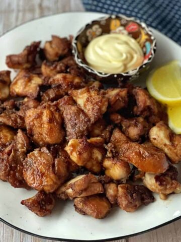 A plate of fried chicken pieces served with lemon wedges and a small bowl of mayonnaise on the side.