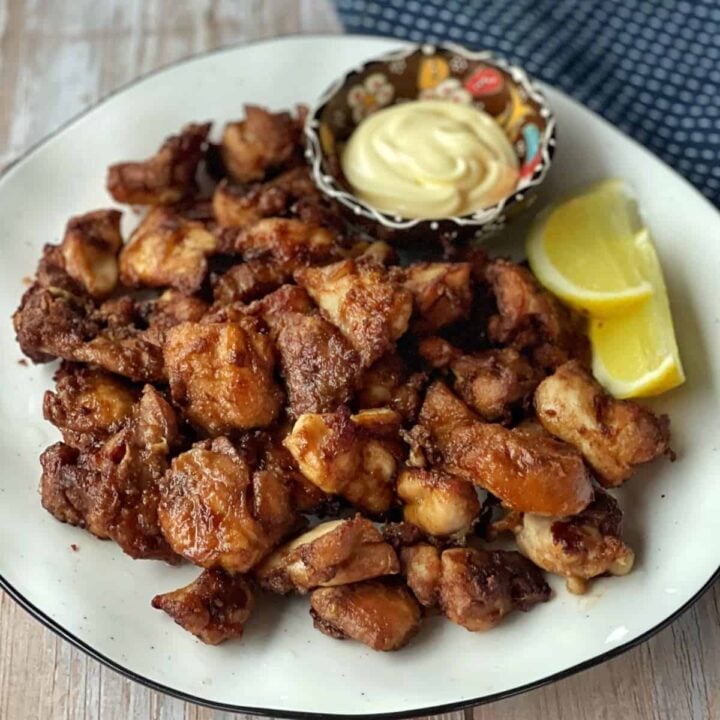 A plate of fried chicken pieces served with lemon wedges and a small bowl of mayonnaise on the side.