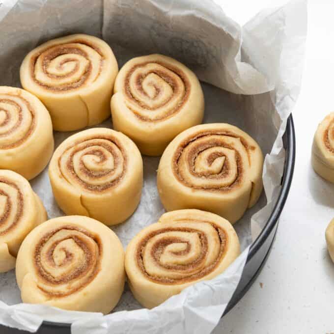Biscoff Cinnamon Scrolls Unbaked cinnamon rolls arranged in a parchment-lined round baking pan, ready to be baked.