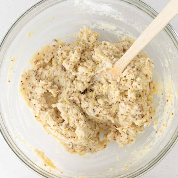 A glass bowl filled with mixed dough and a wooden spoon resting inside.