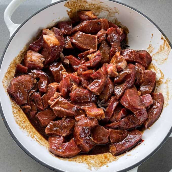5 Spice Beef Chunks of raw beef marinated in a dark sauce sit in a white bowl on a gray countertop.