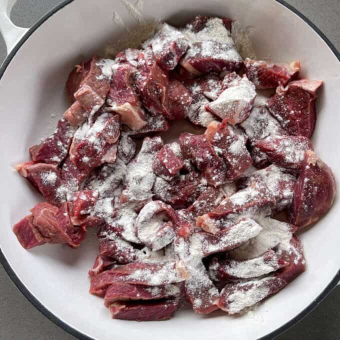 5 Spice Beef Raw beef chunks coated with flour are arranged in a white bowl, ready for cooking.