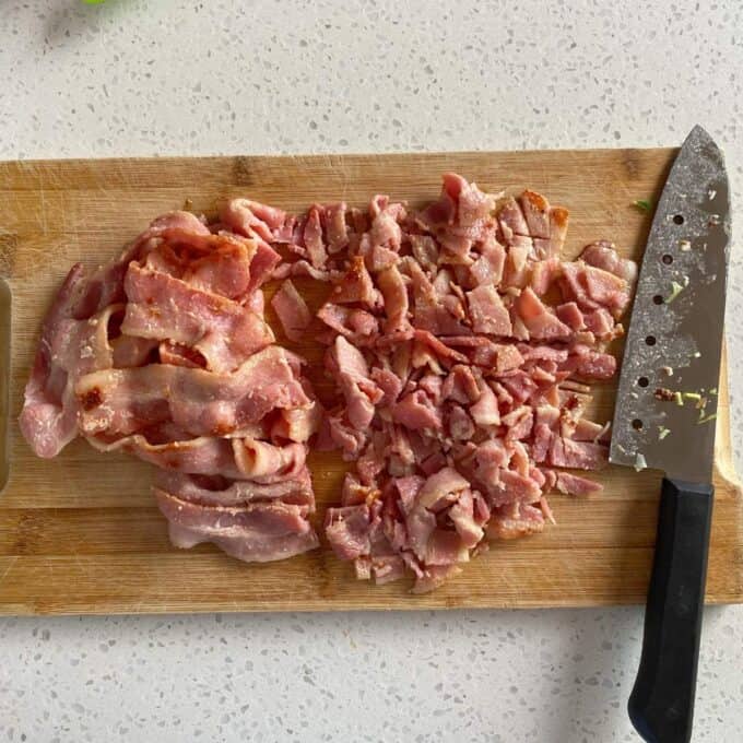 Bacon Veggie Pasta Bake Chopped and sliced raw bacon on a wooden cutting board beside a kitchen knife.