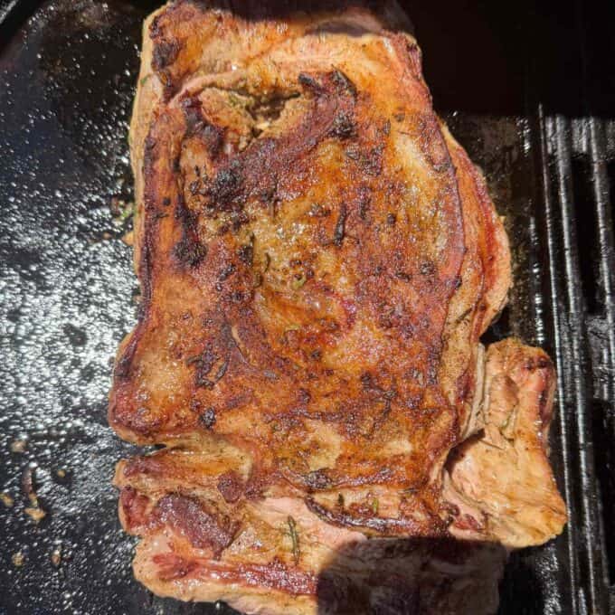 BBQ Lamb with Fresh Mint Sauce A close-up of a cooked steak with grill marks on a dark grill surface.