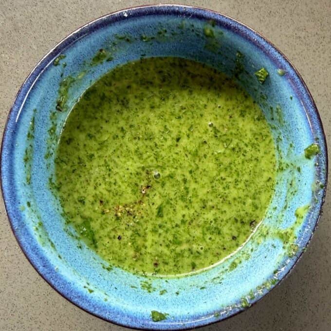 BBQ Lamb with Fresh Mint Sauce A blue bowl containing a green, slightly chunky sauce or dip, sitting on a light-colored surface.