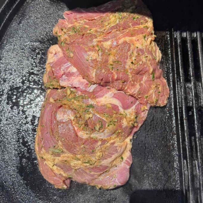 BBQ Lamb with Fresh Mint Sauce Two pieces of seasoned raw meat are placed side by side on a black grill or skillet, ready to be cooked.