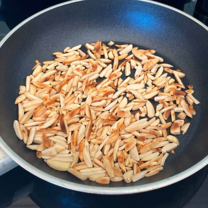 Chicken and Rice Pilaf A nonstick pan containing slivered almonds being toasted, some pieces browned, on a stovetop.