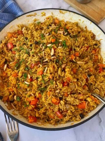 A pan filled with cooked rice mixed with chopped vegetables, herbs, and spices, with a serving spoon on the side.