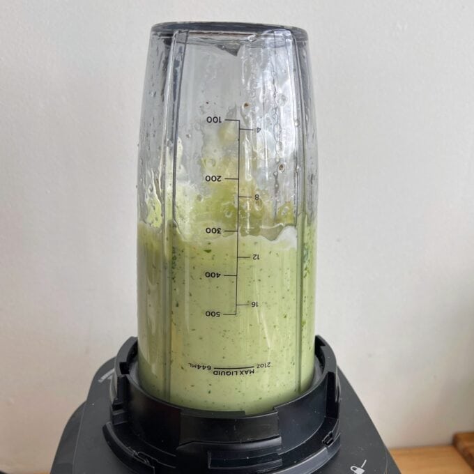 Green Goddess Avocado Salad A blender cup filled with a green smoothie is attached upside down on a blender base, with measurement markings visible on the cup.