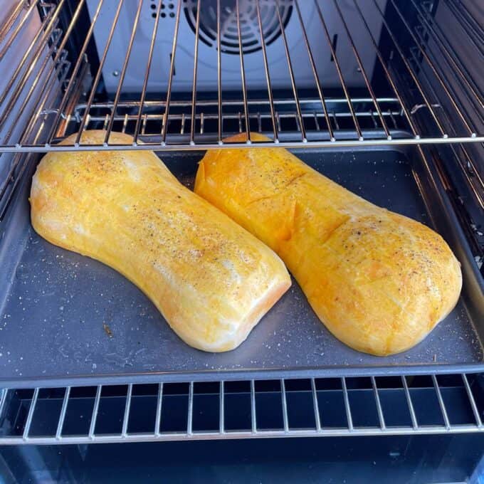 Maple Roasted Hasselback Butternut Two halved butternut squashes, seasoned with salt and pepper, roasting on a baking tray inside an oven.