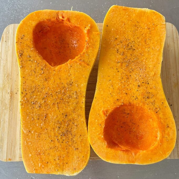 Maple Roasted Hasselback Butternut Two butternut squash halves with seeds removed, seasoned with salt and pepper, placed on a wooden cutting board.