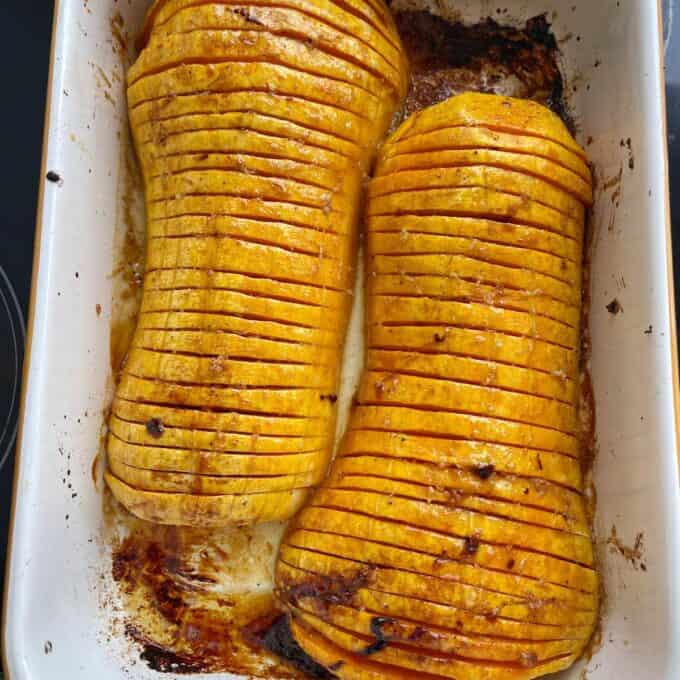 Maple Roasted Hasselback Butternut Two halves of hasselback butternut squash are baked in a white roasting dish, showing thin, even slices and roasted edges.