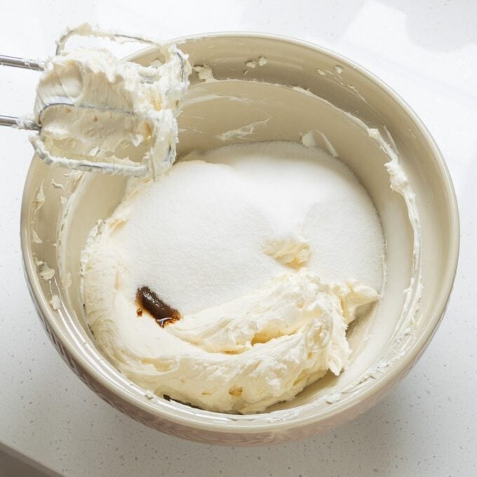 Lemon Blueberry Basque Cheesecake A mixing bowl containing cream cheese, sugar, and vanilla extract with an electric hand mixer resting on the rim.