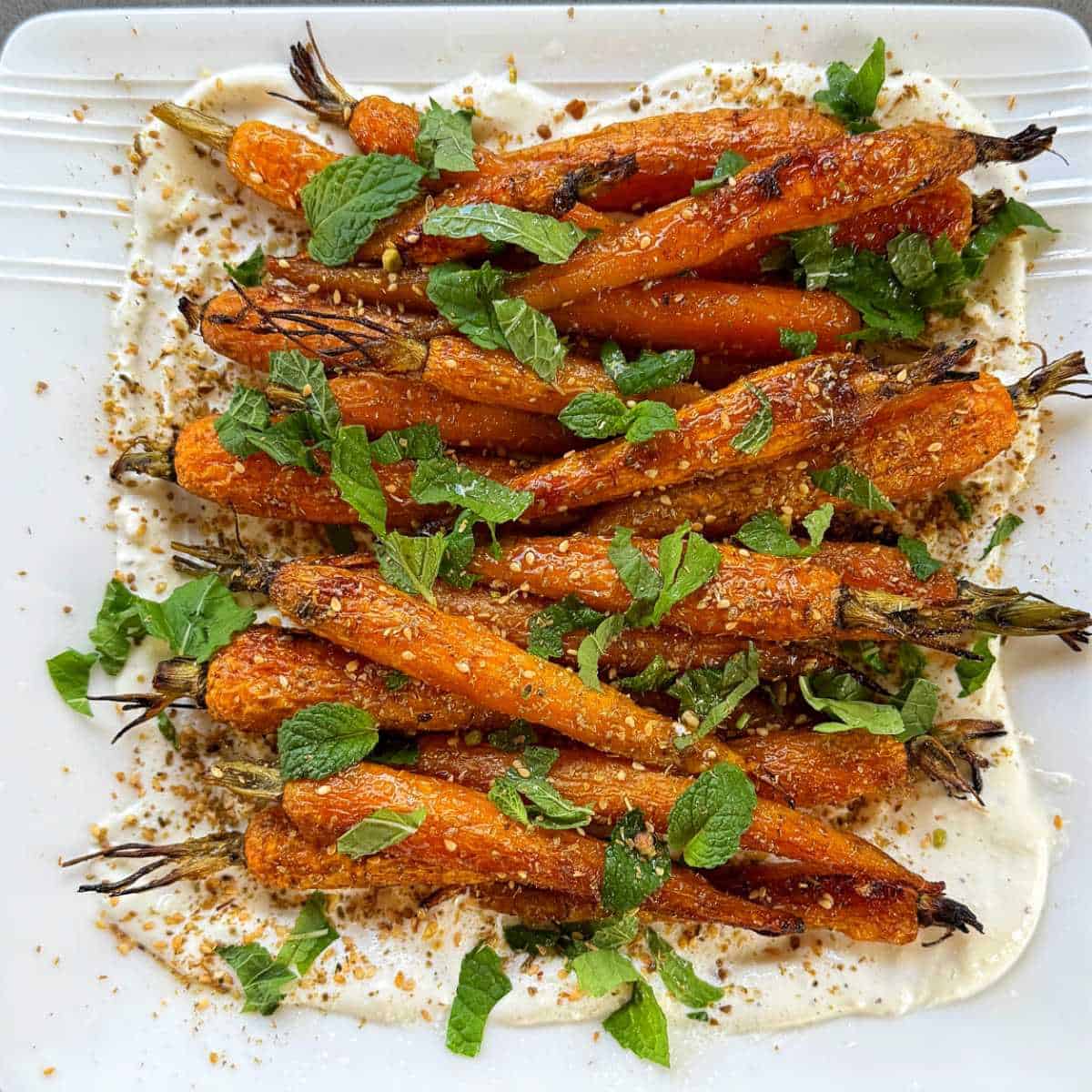 Roasted Carrot with Feta Whip A plate of roasted carrots garnished with fresh mint leaves and spices, served on a layer of creamy white sauce.