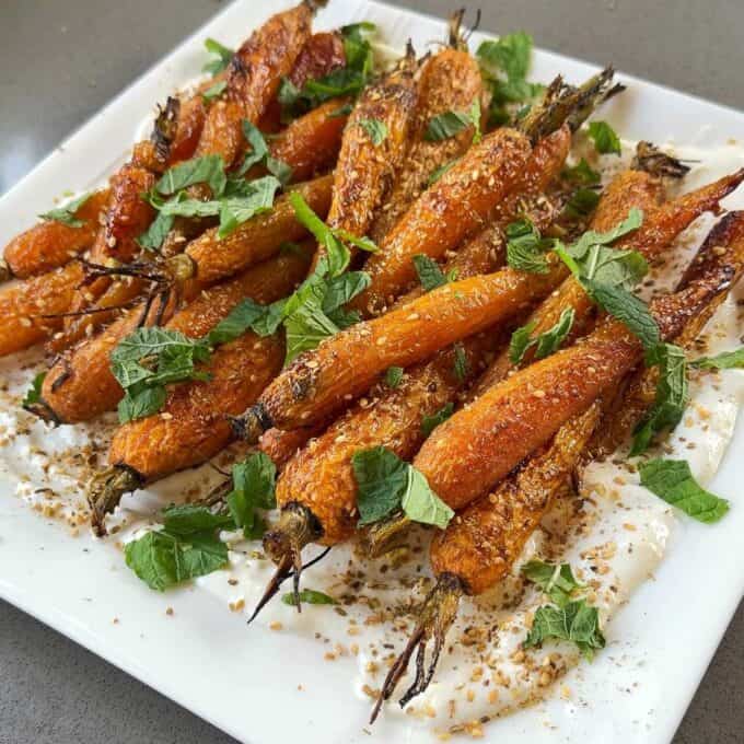Roasted Carrot with Feta Whip Roasted carrots with seasoning served on a white plate, garnished with fresh herbs and laid over a spread of creamy sauce.