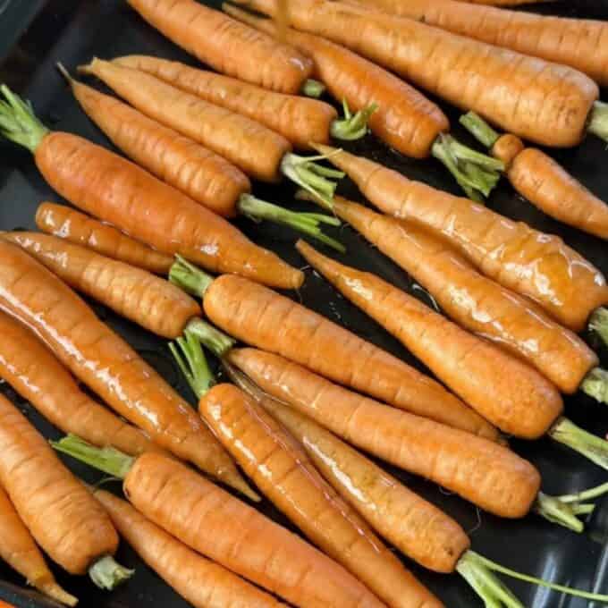 Roasted Carrot with Feta Whip A tray of whole, raw carrots with stems, coated in oil and arranged in a single layer, ready for roasting.