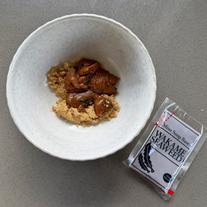 BBQ Miso Eggplant A white bowl contains brown miso paste and mushrooms. Next to the bowl is a packet labeled Wakame Seaweed Miso Soup Base.