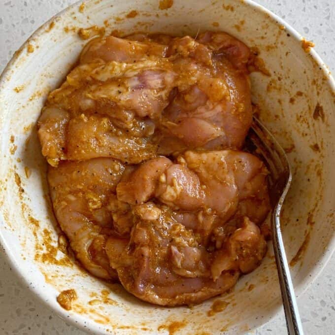 Chipotle Chicken Tostadas Raw chicken pieces marinated with spices in a white bowl, with a fork resting on the side.