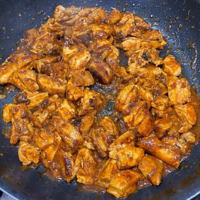 Chipotle Chicken Tostadas Cooked pieces of chicken coated in a reddish-brown sauce in a frying pan.