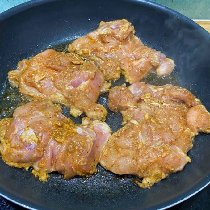 Chipotle Chicken Tostadas Raw marinated chicken pieces cooking in a black frying pan.