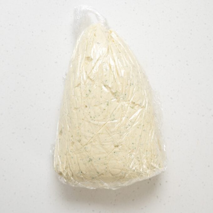 Christmas Cheeseball A mound of dough wrapped in plastic wrap sits on a white speckled surface.