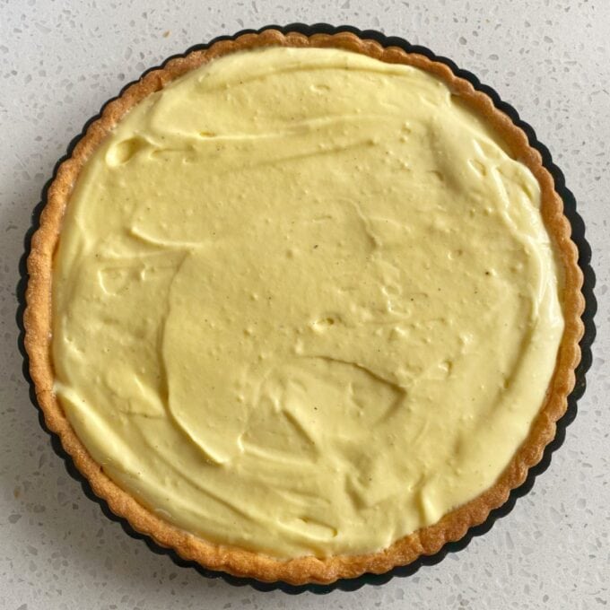 Fresh Berry Custard Tart A tart with a golden-brown crust filled with smooth, creamy yellow custard, set on a light-colored speckled surface.