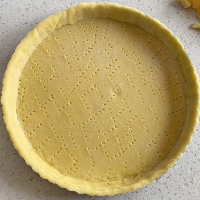 Fresh Berry Custard Tart Unbaked tart crust with fork holes in a round baking tin on a light countertop.