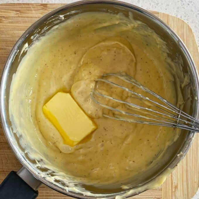 Fresh Berry Custard Tart A saucepan with thick yellow custard, a pat of butter, and a metal whisk on a wooden cutting board.