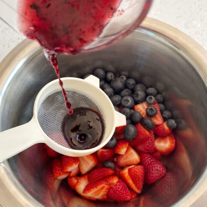 Fresh Berry Custard Tart A person pours berry juice through a strainer into a bowl of fresh strawberries and blueberries.