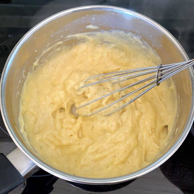 Fresh Berry Custard Tart A whisk in a saucepan with thick, creamy mashed potatoes on a stovetop.