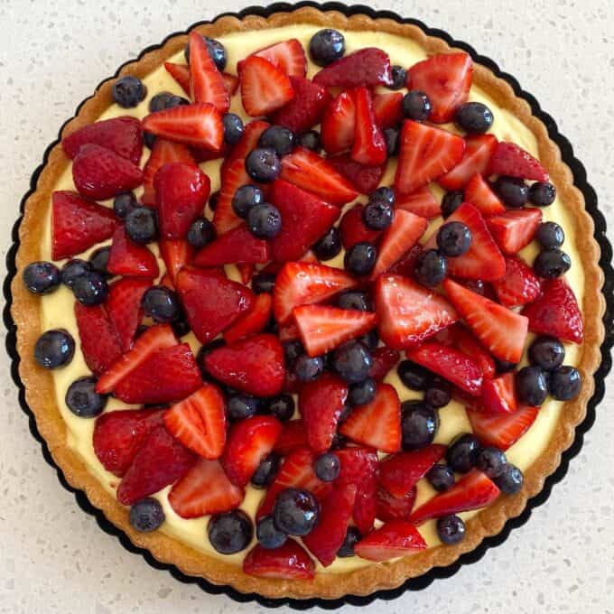 Fresh Berry Custard Tart A fruit tart with a pastry crust, cream filling, and topped with fresh strawberries and blueberries, presented on a light-colored surface.
