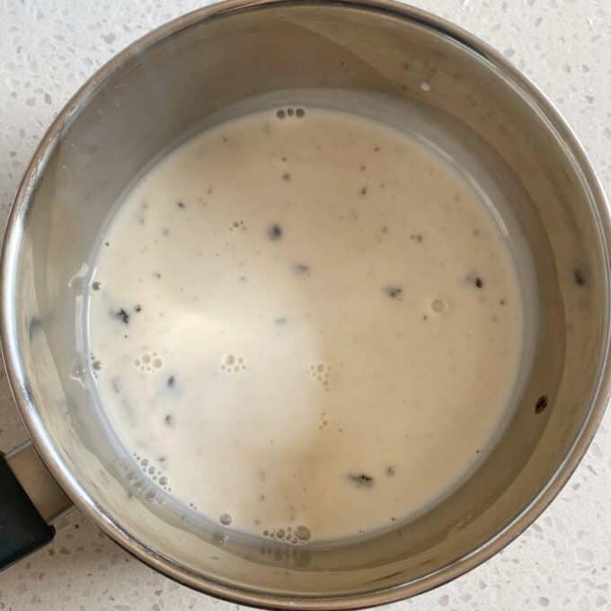Fresh Berry Custard Tart A metal saucepan containing a creamy white liquid with small black specks, placed on a light-colored countertop.