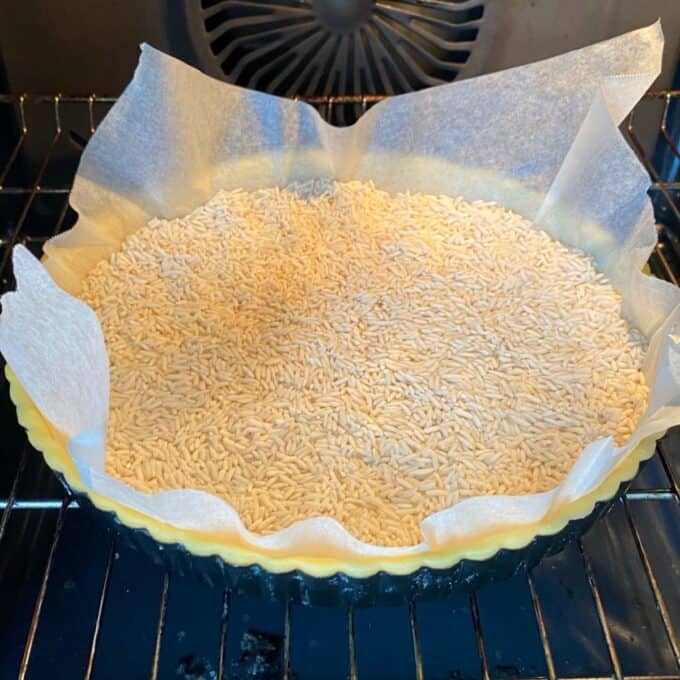 Fresh Berry Custard Tart Unbaked tart crust lined with parchment paper and filled with dry rice for blind baking, placed in an oven.