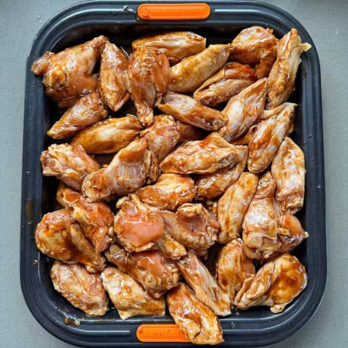 Honey Chicken Nibbles A tray filled with raw chicken wings coated in a brown marinade, arranged in a single layer and ready for cooking.